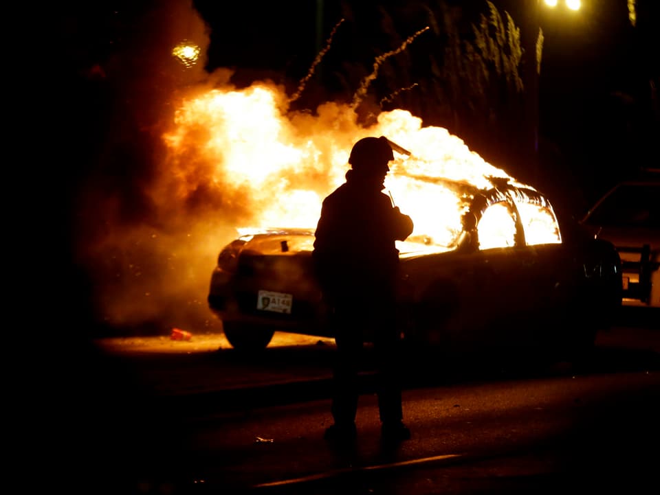 Feuerwehrmann steht vor brenndem Polizeiwagen