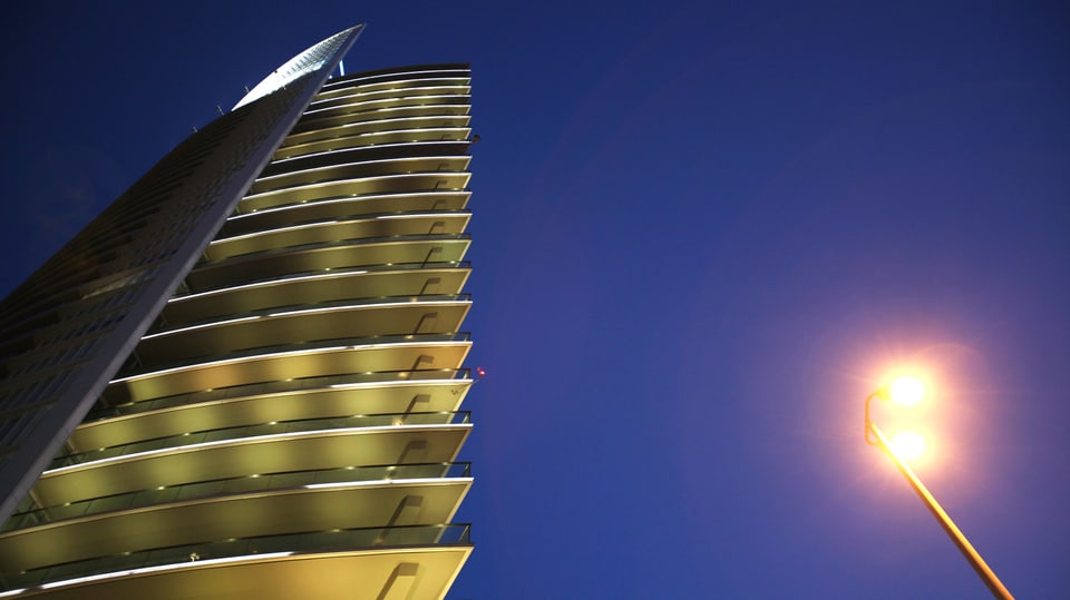 Ein 26-stöckiger Turm ragt in den Himmel, rechts im Bild eine brennende Laterne.