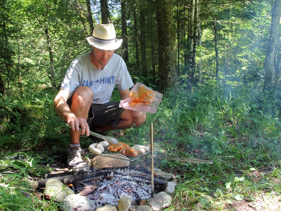 Mann steht am Feuer und legt Fleisch auf dem Grill.