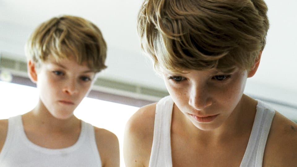Zwei Jungen in weissen Unterhemden, konzentriert nach unten blickend.