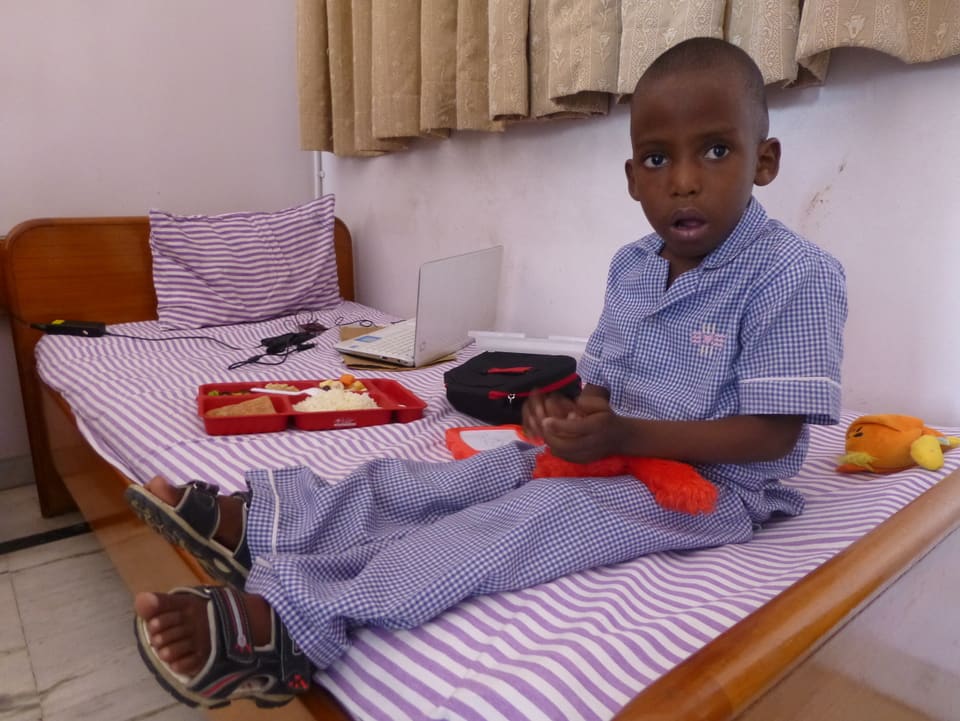 Ein fünfjähriger Knabe ist aus Nigeria sitzt auf einem Bett in Shettys Klinik.