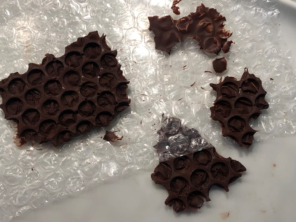 Auf einer Plastikfolie liegen Schokolade-Stücken. Diese werden zur Dekoration von Desserts gebraucht. 
