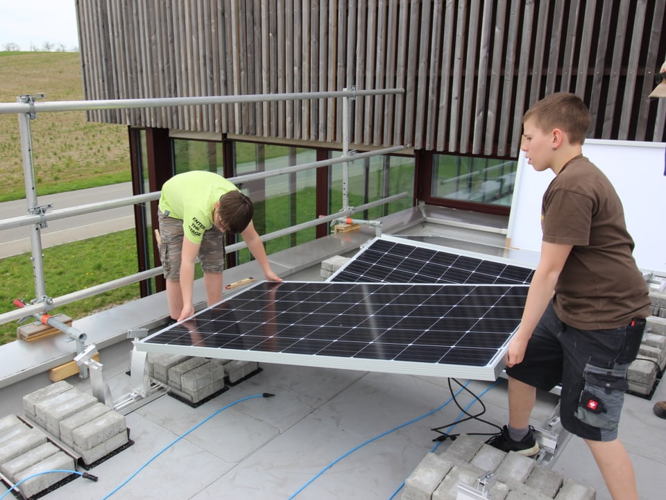 Zwei Sekundarschüler aus Marthalen montieren ein Solarpanel auf dem Dach ihrer Schule.