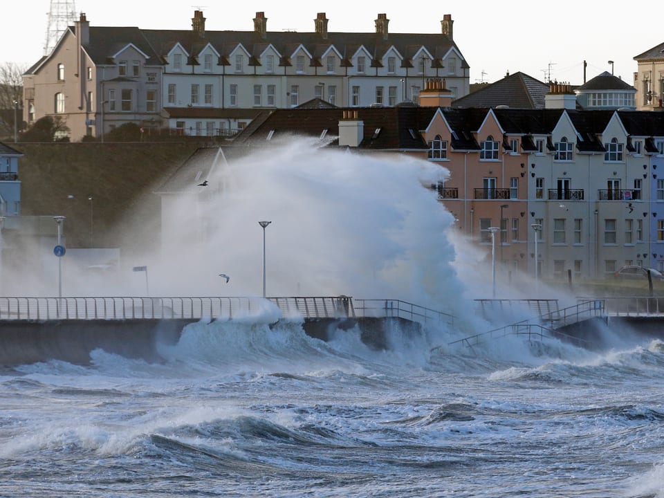 Hohe Wellen überfluten Küstenpromenade eines irischen Städtchens.