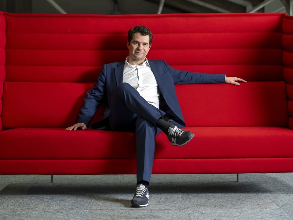 Jérôme Thiriet sitzt auf einem grossen, roten Sofa.