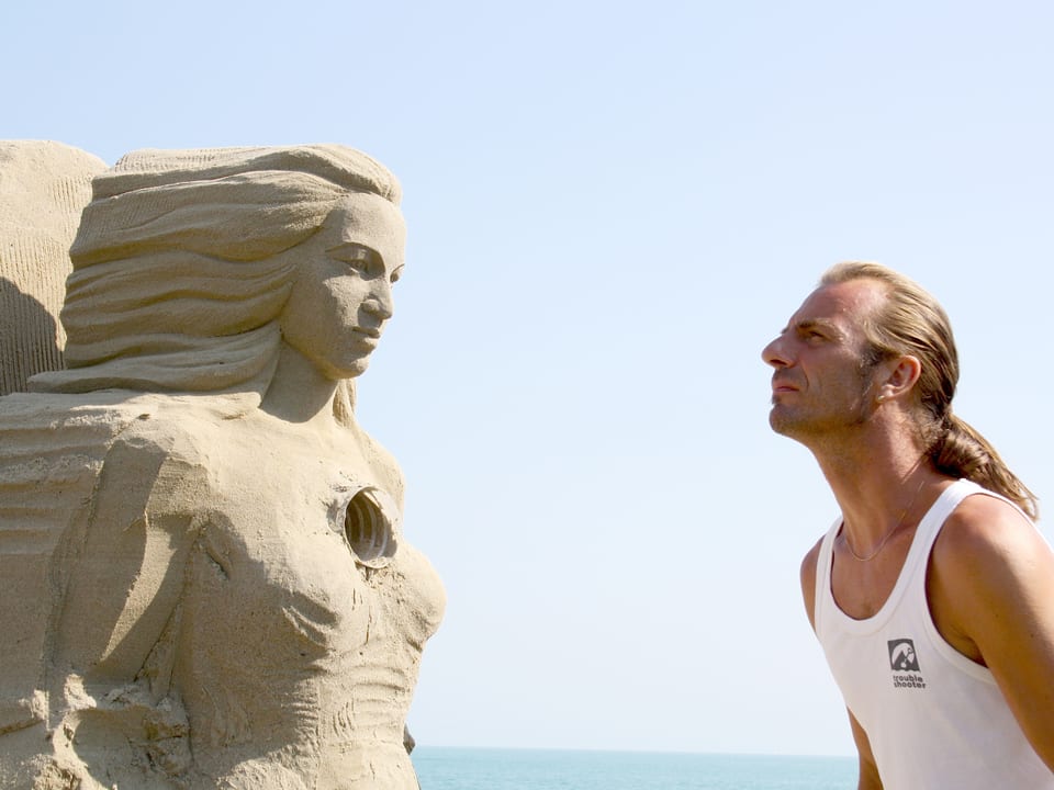 Ein Mann steht einer Sandskulptur gegenüber und schaut sie an.