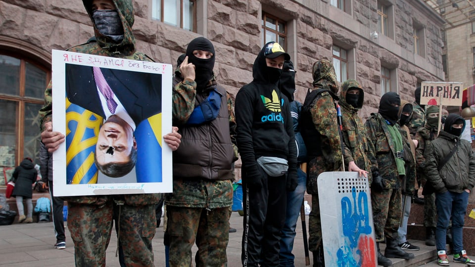 Vermummte Demonstranten vor dem Rathaus in Kiew, einer hält ein Portrait des Präsidenten verkehrt herum.