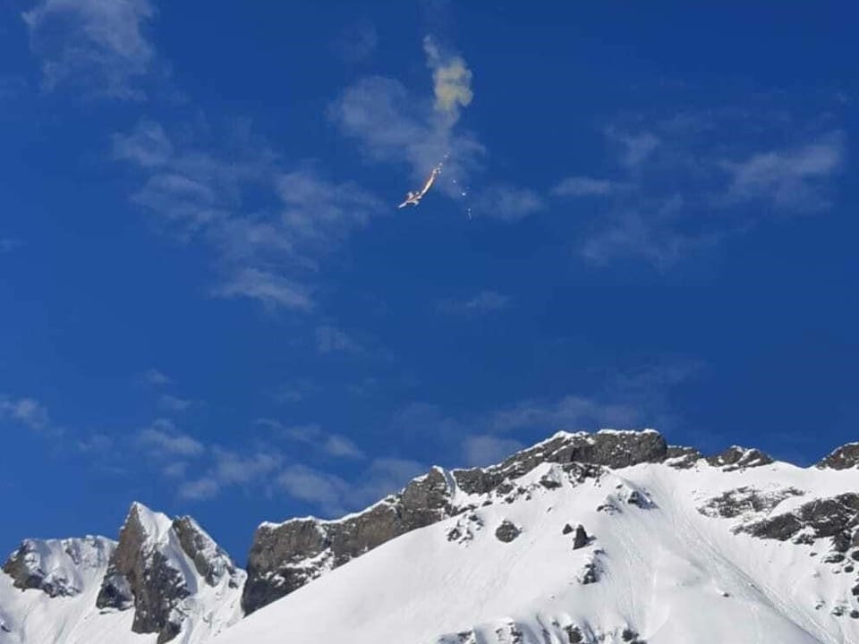 Der Absturz der F5 Tiger Maschine auf der Melchsee-Frutt. Flammen, Rauch und der Fallschirm des Piloten sind sichtbar.
