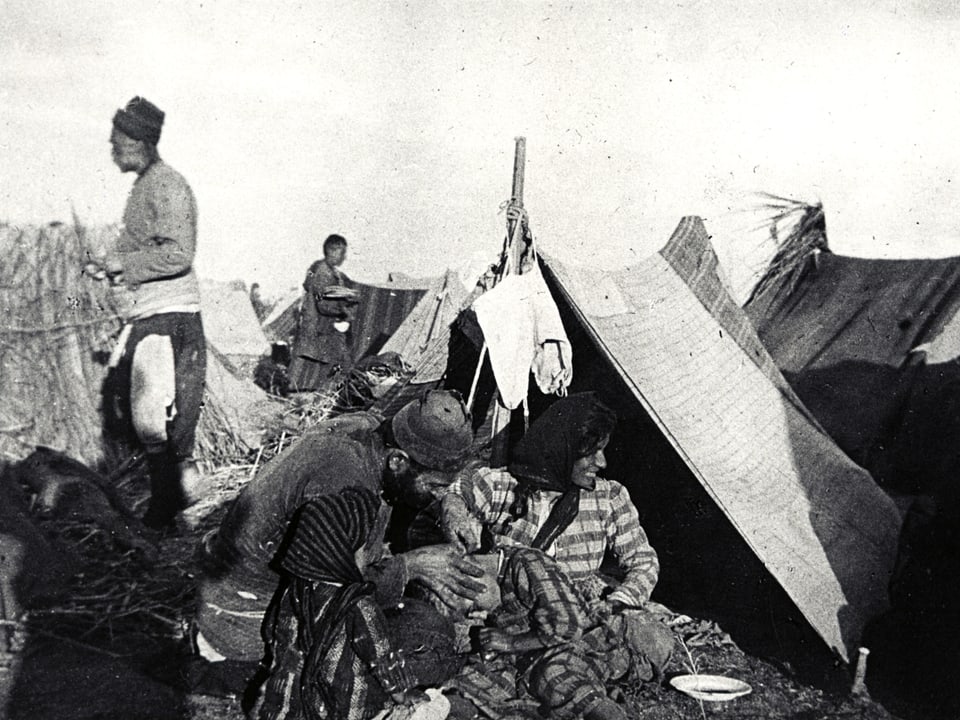 Altes Foto von Menschen, die vor einem Zelt sitzen.