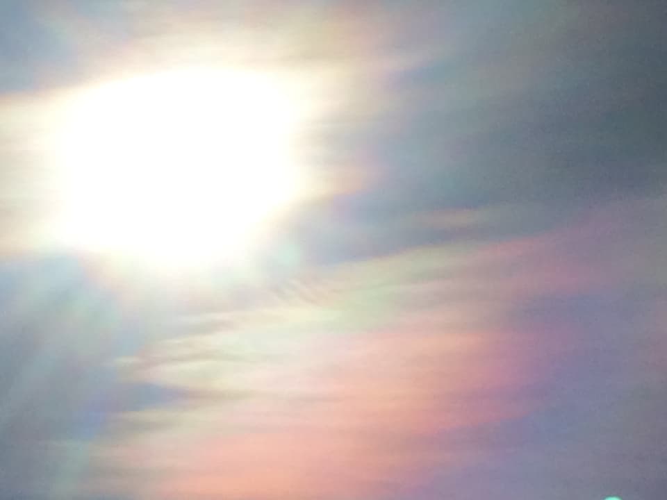 Perlmutfarbene Wolken neben der Sonne.