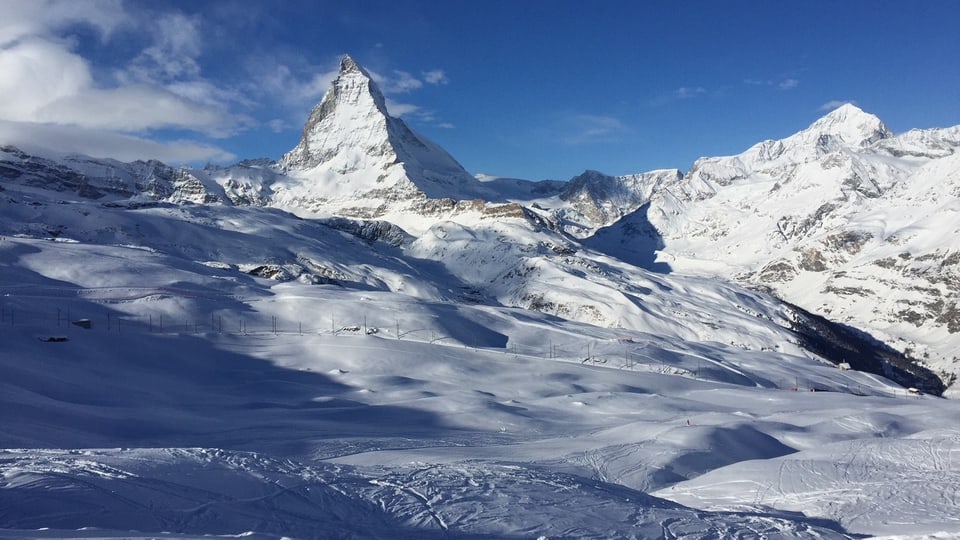 Matterhorn in der Ferne, davor schneebedeckte Hänge und Skispuren.