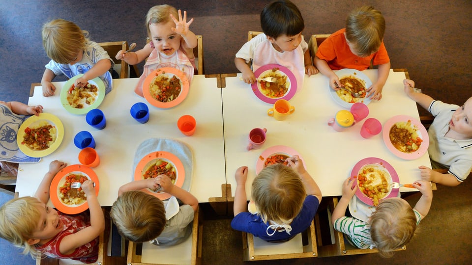 10 Kinder essen an einem Tisch.