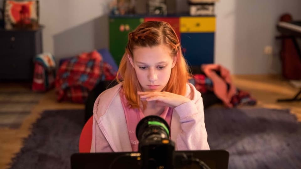 Ein Mädchen sitzt im Kinderzimmer vor der Webcam.