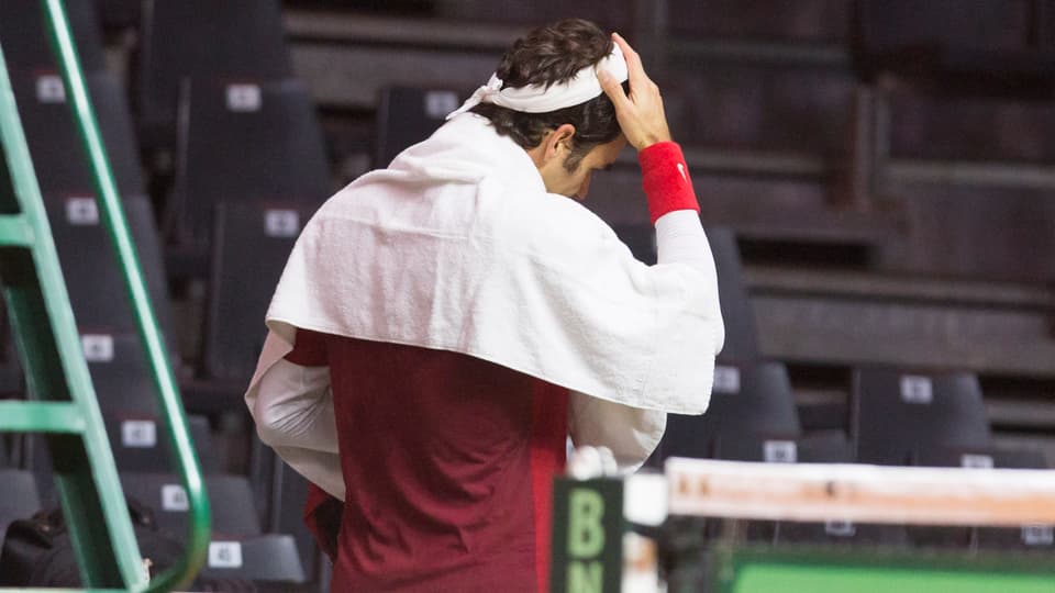 Roger Federer, von hinten aufgenommen, fasst sich mit einem Tuch um die Schultern an den Kopf.