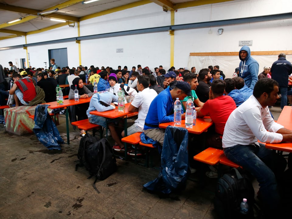 Flüchtlinge sitzen an langen Tischen im Erstaufnahmezentrum. 