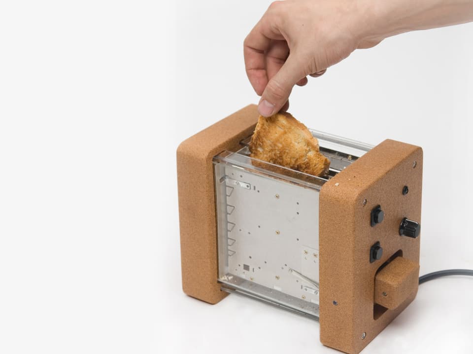 Ein Toaster mit einer Hülle aus Kork, aus dem gerade eine Hand ein getoastetes Brot fischt.