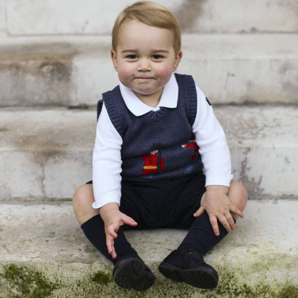 Prinz George in kurzen Hosen auf einer Steintreppe sitzend.