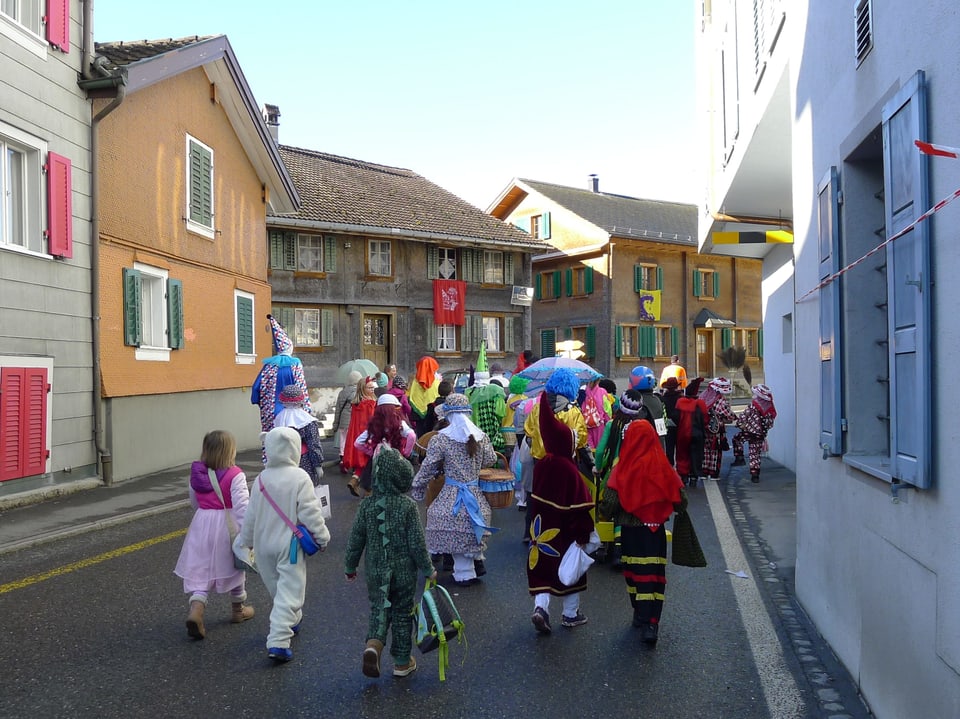 Eine Gruppe verkleideter Kinder marschiert an einem Fasnachtsumzug durch ein Dorf. 