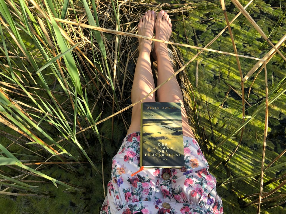 Der Roman «Der Geang der Flusskrebse» von Delia Owens liegt auf Annette Königs Beinen