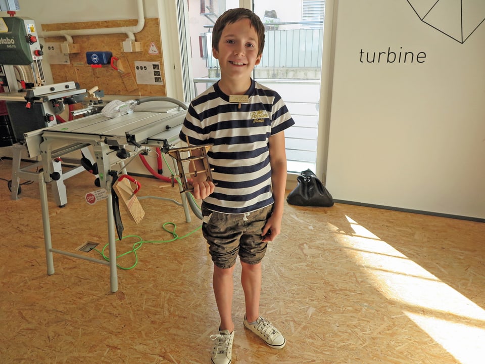 Ein Junge zeigt stolz seine selbstgebasteltes Mobil aus Holz. 