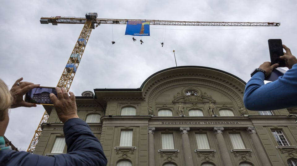 Zwei Personen fotografieren mit ihren Handys die Aktivisten und ihr Transparent