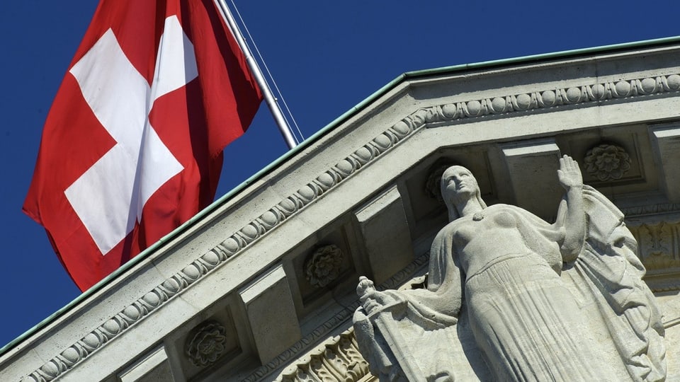Schweizer Flagge vor dem Bundesgerichts-Gebäude mit Helvetia-Skulptur.