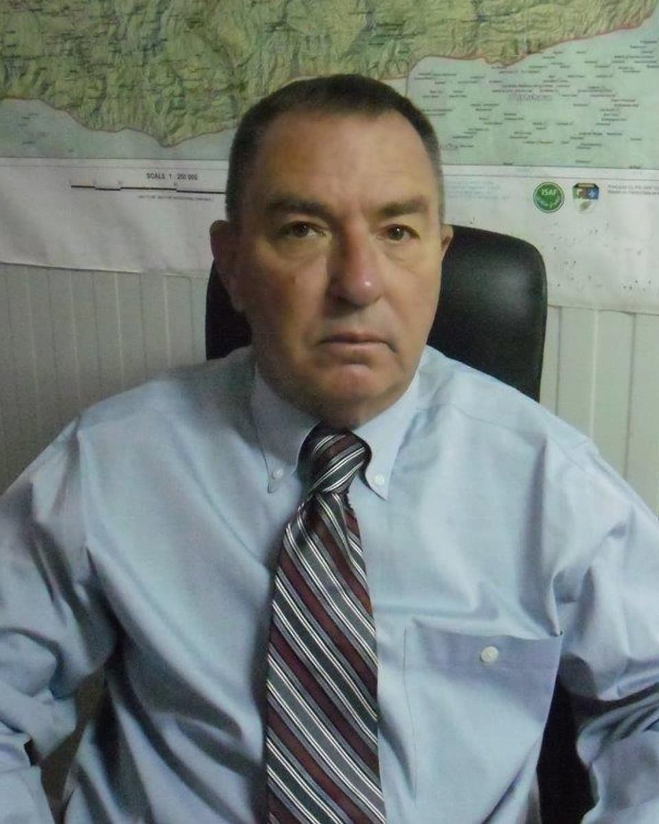 Der Militarstratege Gary Anderson in Hemd und Krawatte sitzend vor einer Landkarte an der Wand.