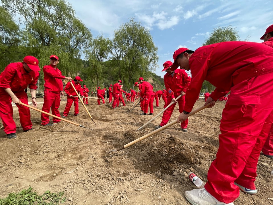 Teambuilding-Aktivität: Angestellte in roten Anzügen graben einen Acker um.