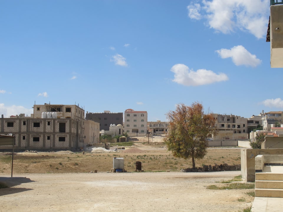 Blick auf ein Wohnquartier in Jordanien. Karge Landschaft und blauer Himmel mit Wolken.