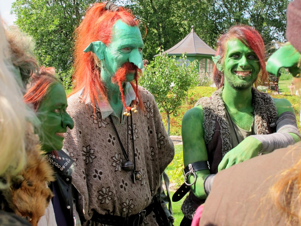 Menschen, grün angemalt, mit orangen Haaren und spitzen Ohren