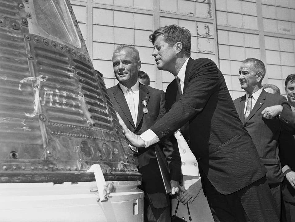 John F. Kennedy (Mitte) schaut in die Mercury-Kapsel, daneben John Glenn (links) und Lyndon B. Johnson (rechts)