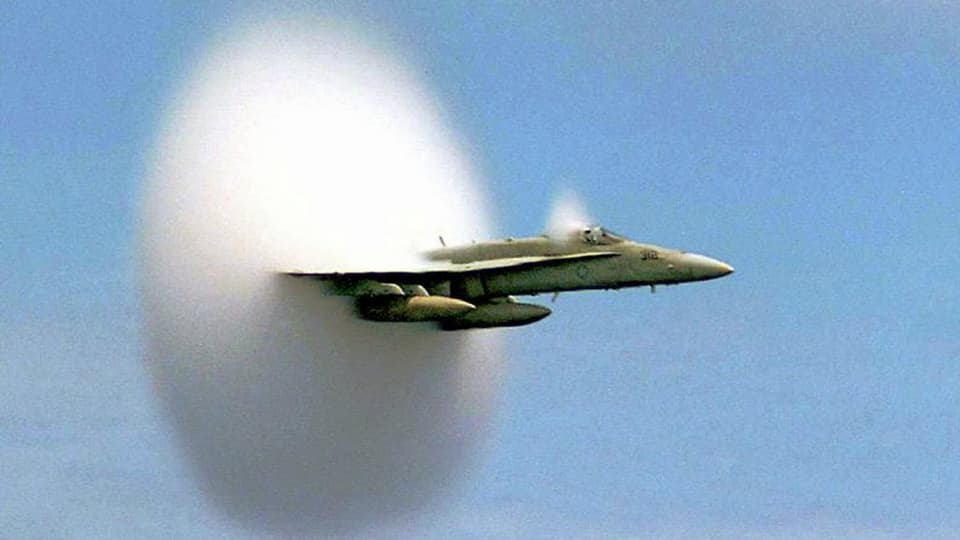 Kampfjet fliegt durch die Schallmauer, welche sich als eine Art Wolke zeigt.