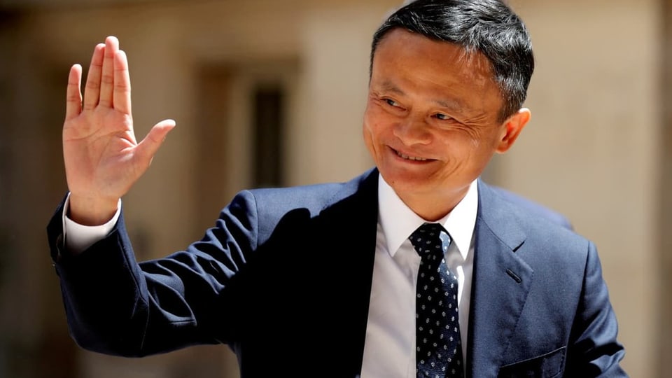 Jack Ma in Nahaufnahme: er hebt die rechte Hand gestreckt, grüsst und lächelt.