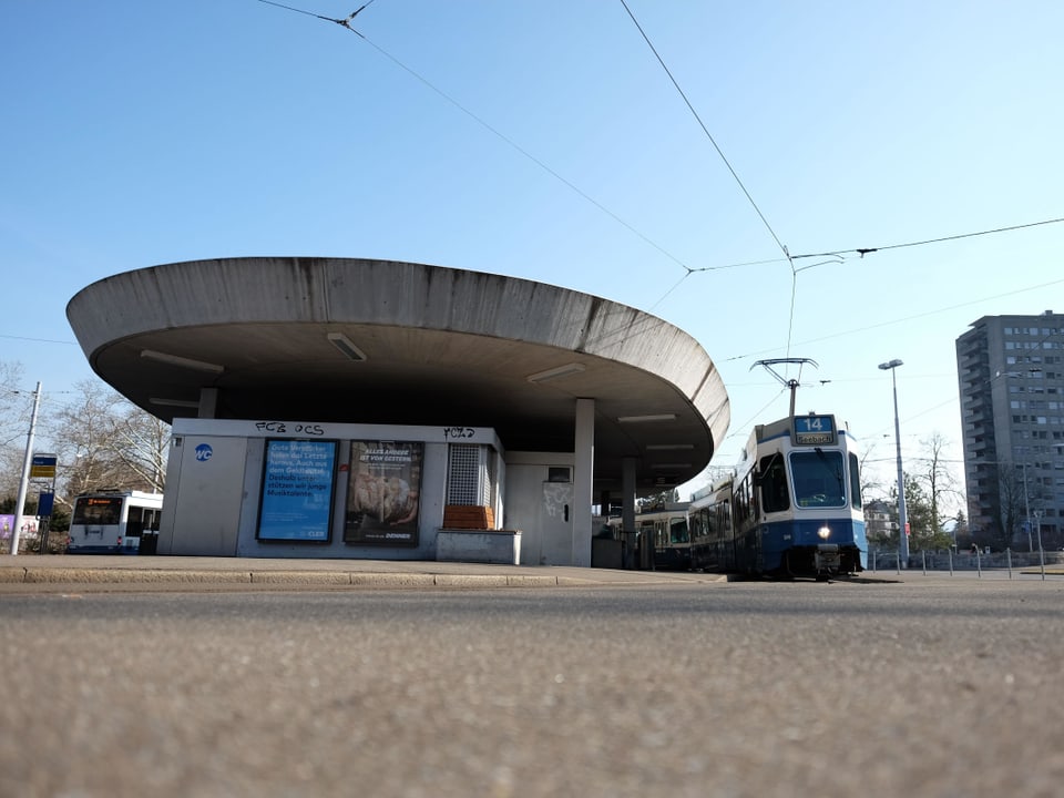 Ein blau-weisses Tram steht an der Endhaltestelle mit ovalförmigem Betondach.