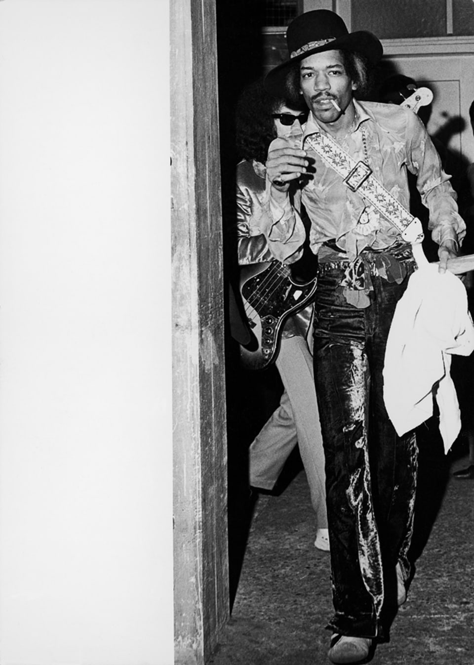 Jimi Hendrix kommt mit Zigarette im Mund zu einer Tür herein. 