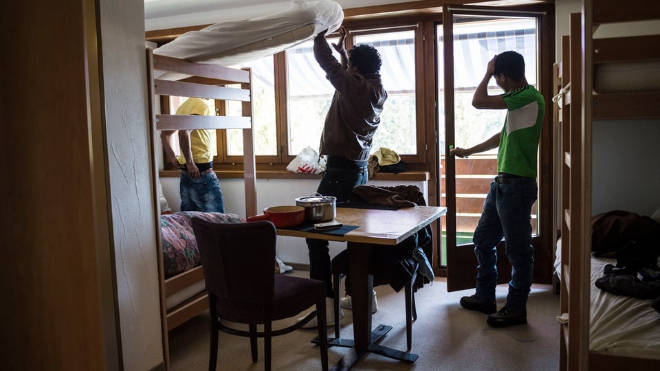 Drei Asylsuchende in einem kleinen Zimmer mit Kajütenbetten.