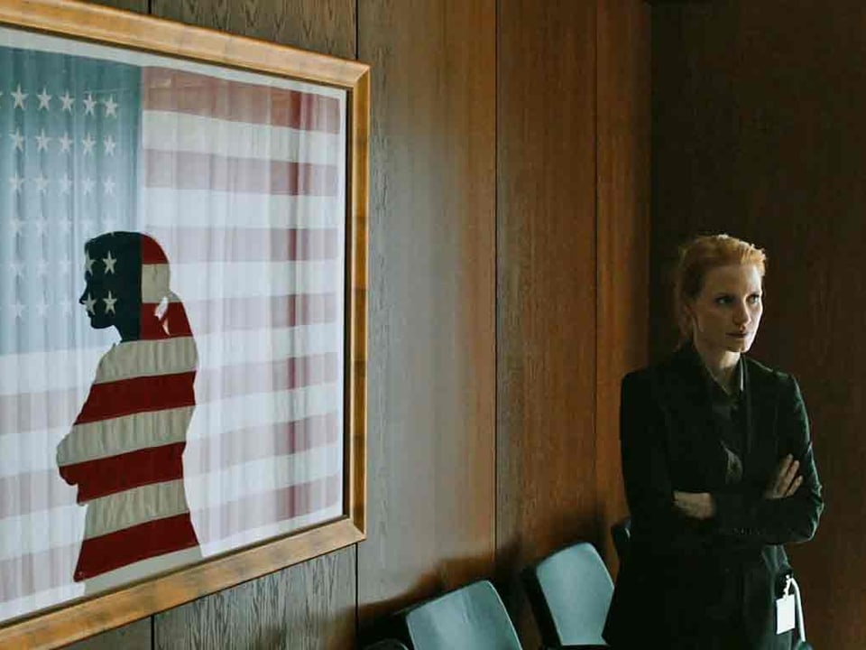 Die Schauspielerin spiegelt sich in der Glasscheibe einer eingerahmten Amerikanischen Flagge.
