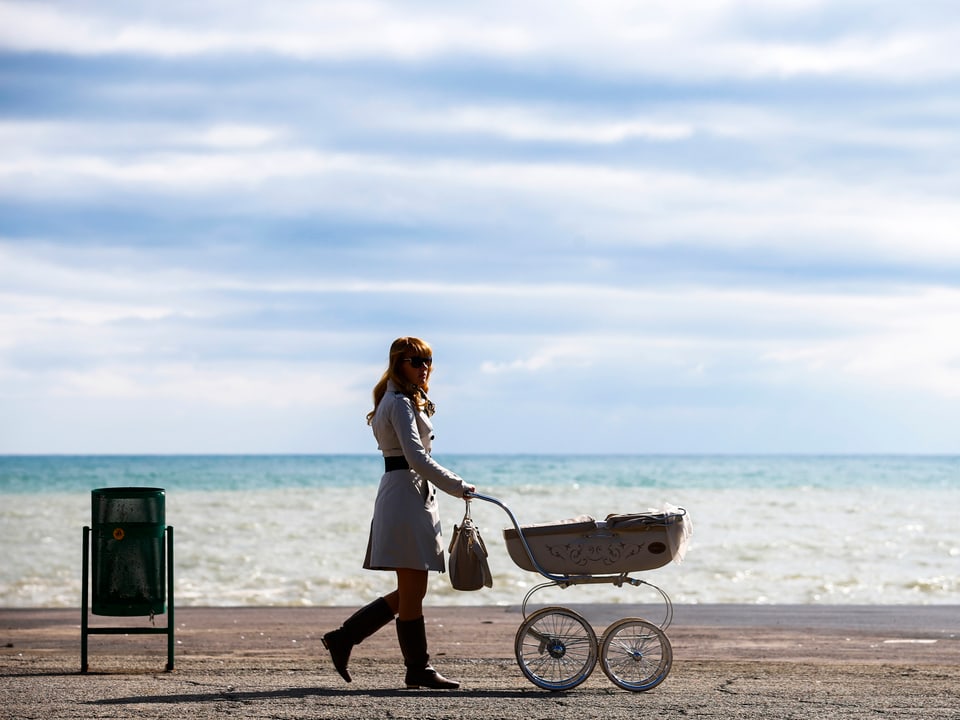 Frau mit Kinderwagen spaziert am Meerufer in der Ukraine.