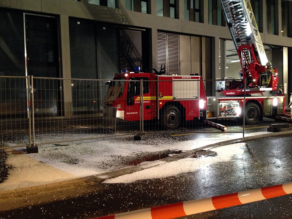 Feuerwehrauto mit Drehleiter auf der Seite des Gebäudes, im Vordergrund Absperrung und Glasscherben.