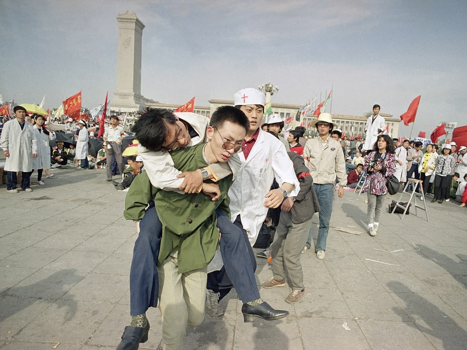 Ein junger Mann trägt einen geschwächten Kollegen vom Tiananmen weg.