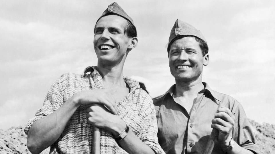 Zwei Männer mit Soldatenhut grinsen in die Kamera.