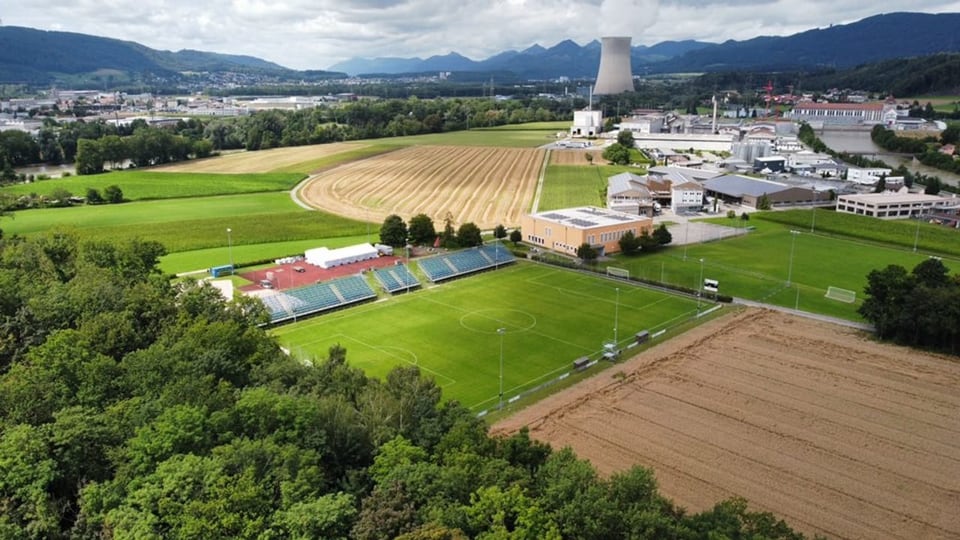 Fussballplatz mit Tribüne. Im Hintergrund AKW-Kühlturm.