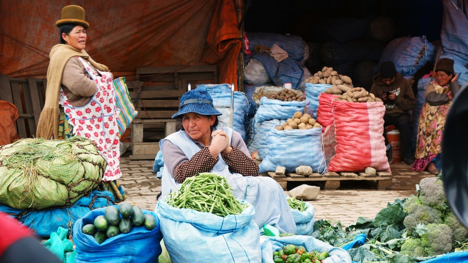 Eine Marktfrau in boliviarischer Kleidung sitzt mit Handelsware am Strassenrand.