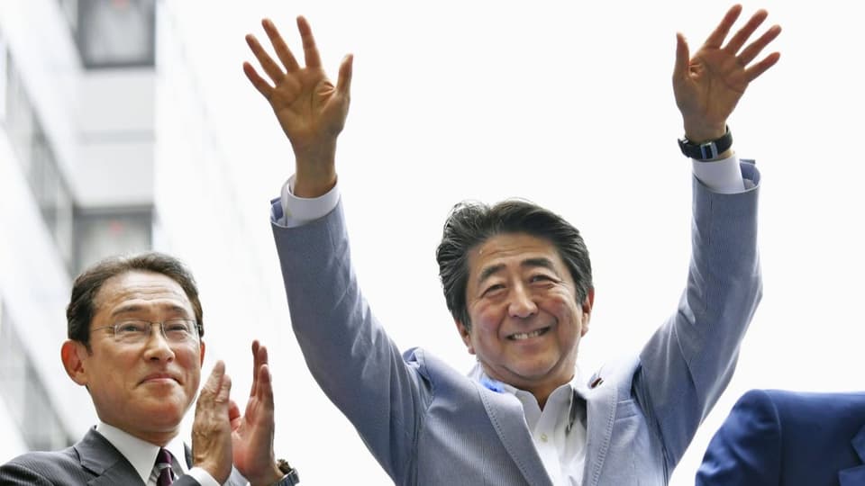 Shinzo Abe jubelt mit hochgestreckten Armen, Fumio Kishida klatscht daneben in die Hände.
