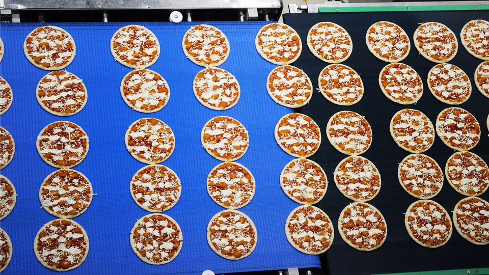 Blick auf ein Laufband bei der automatisierten Herstellung von Tiefkühlpizzas