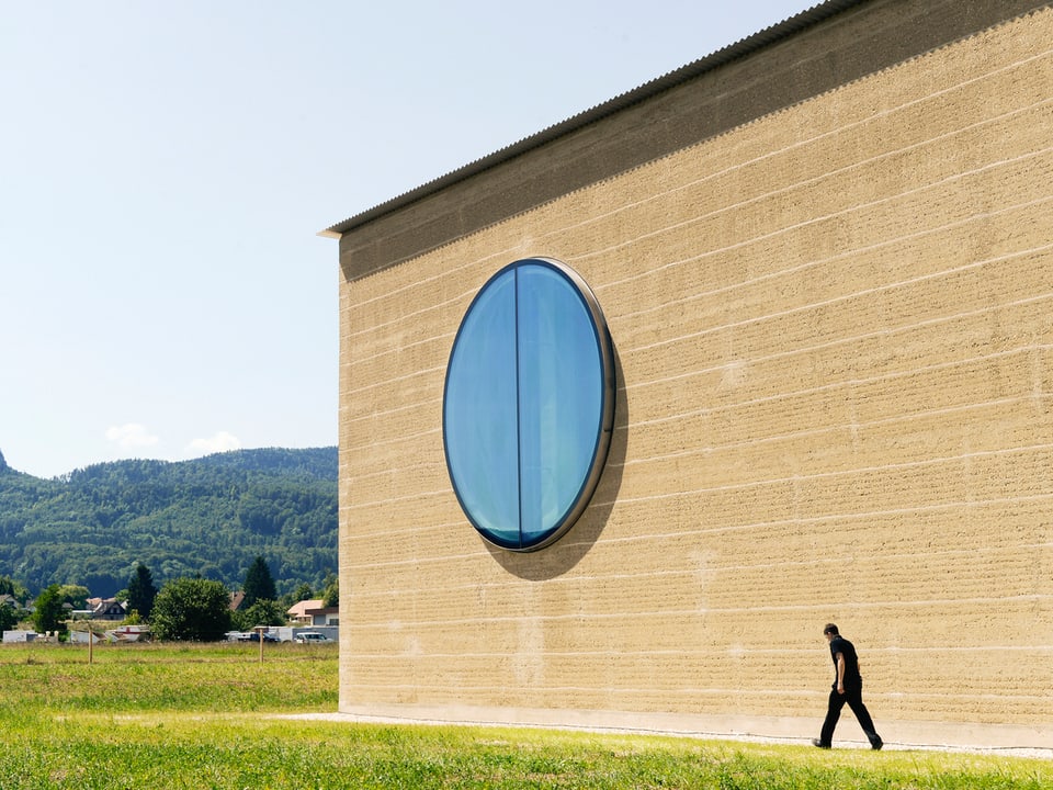 Schlichtes Lehmhaus mit einem grossen, runden Fenster.