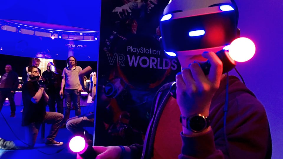 Ein Mann spielt mit einer Virtual Reality Brille und bunten Controllern in der Hand.