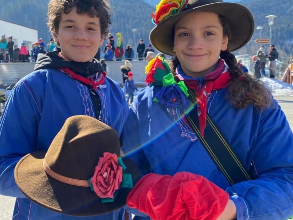 Luan und Nora halten einen brauen Hut bzw. eine rote Mütze in der Hand und lächeln in die Kamera.