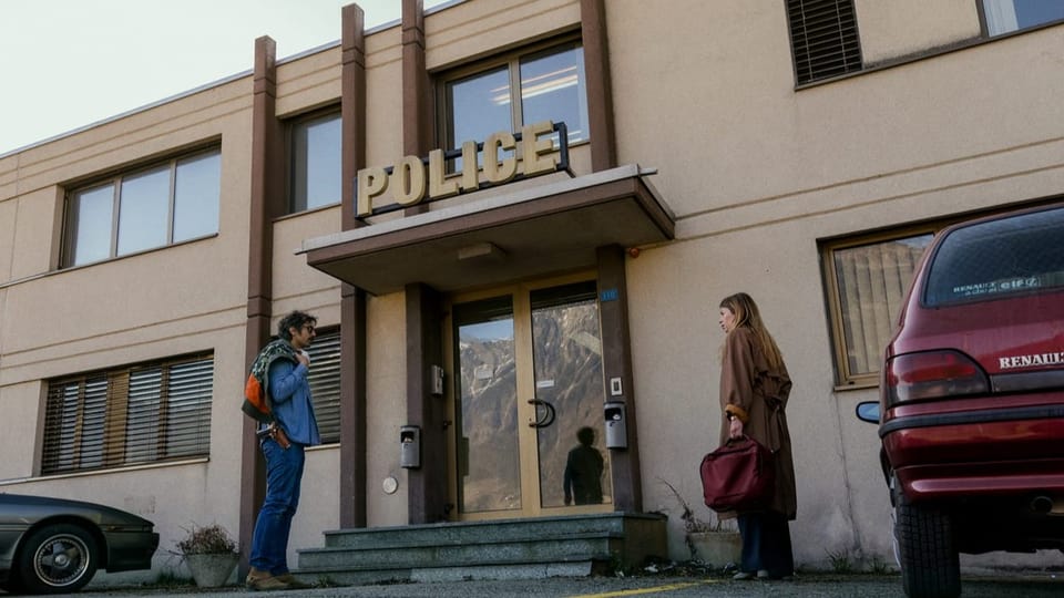 Frau mit roter Tasche trifft Mann mit Sonnenbrille vor Polizeiwache-