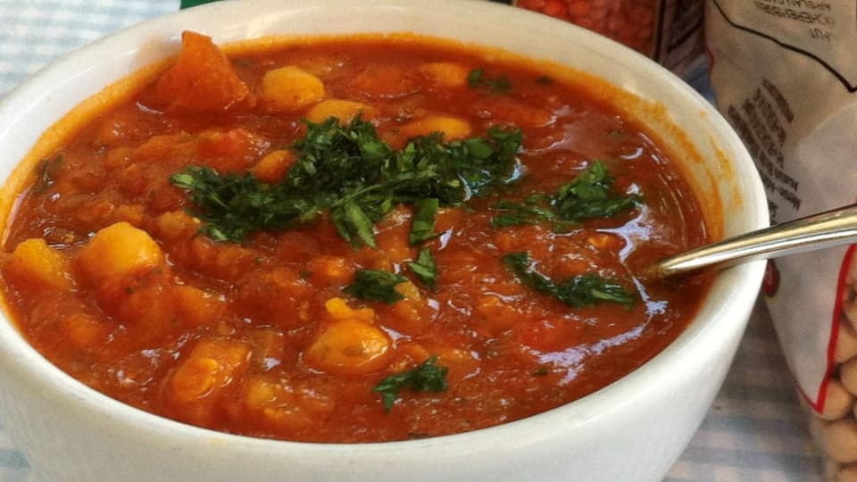 A bowl of chickpea soup with tomato.